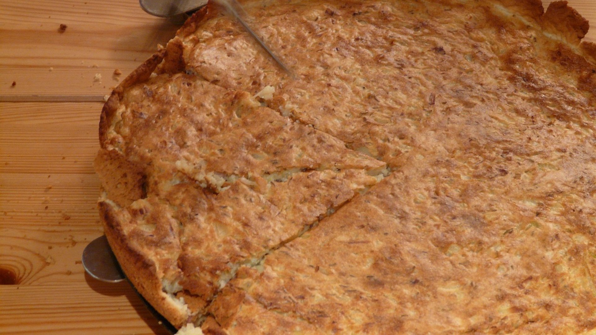 Frisch gebackener Zwiebelkuchen in der Springform, angeschnitten und mit einem Tortenheber serviert