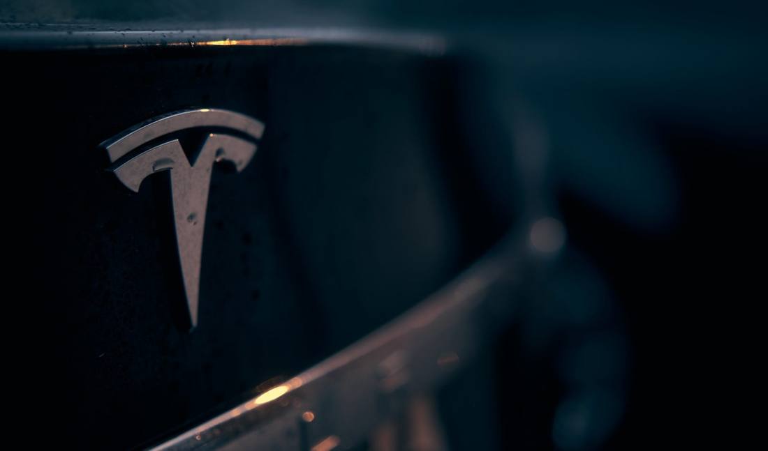 Nahaufnahme des Tesla-Emblems an einem dunklen Fahrzeug