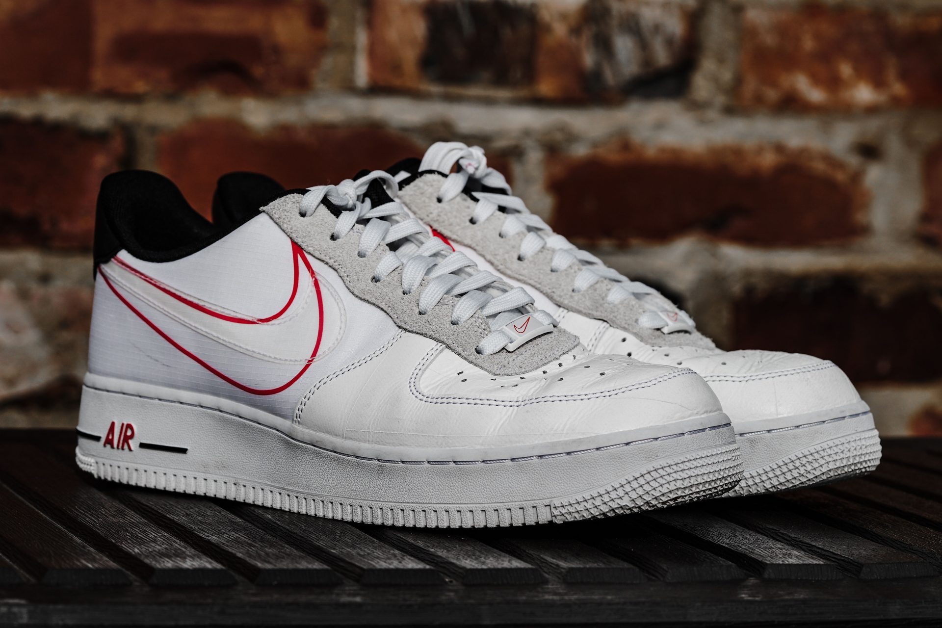 Nike Air Force 1 Sneaker in Weiß mit rot umrandetem Swoosh-Logo vor einer Backsteinwand