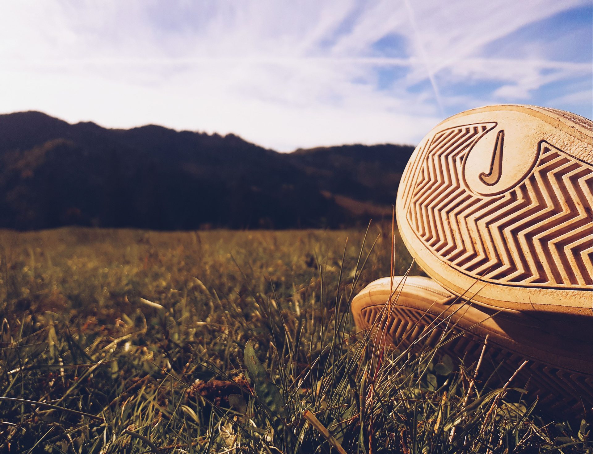 Nike-Sneaker-Sohle mit sichtbarem Swoosh-Profil, fotografiert bodennah in einer Wiese mit Bergen im Hintergrund